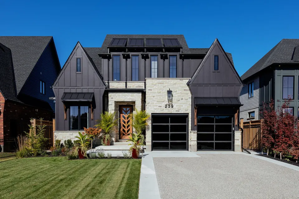 Front elevation of 239 Foxborough Place: charcoal board-and-batten, limestone, black-framed windows and a chevron wood front door under a blue sky