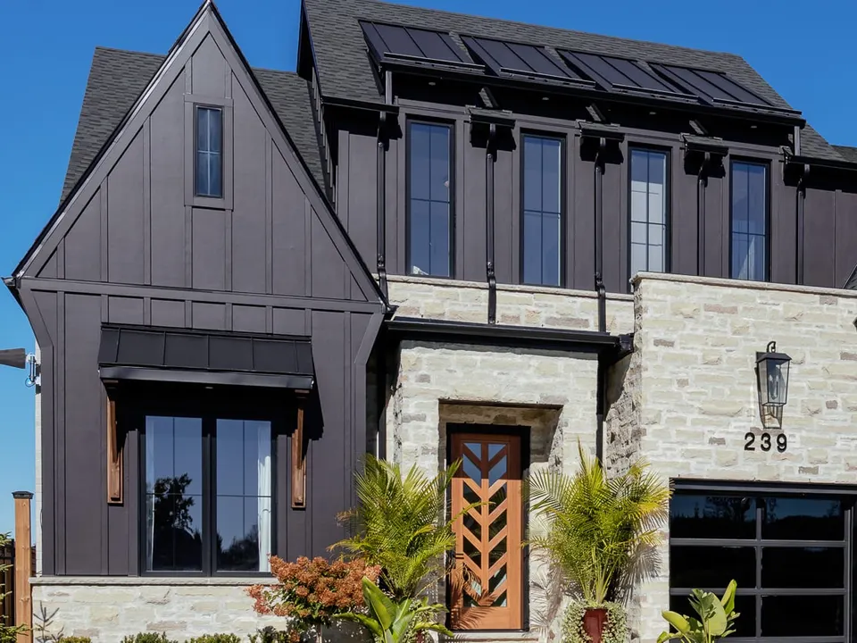 Close view of the front: charcoal board-and-batten gable, metal awning, smeared stone with white mortar, the chevron front door and the lantern beside the 239