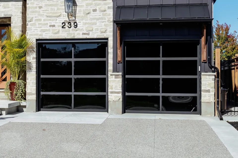 Black glass garage doors, the stone facade and the exposed aggregate driveway