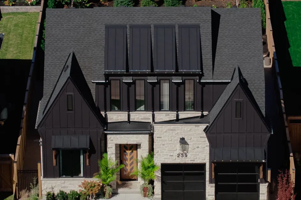 Aerial view of the front of the home: board-and-batten gables, stone entry and metal accent roofs over the window bay and garage