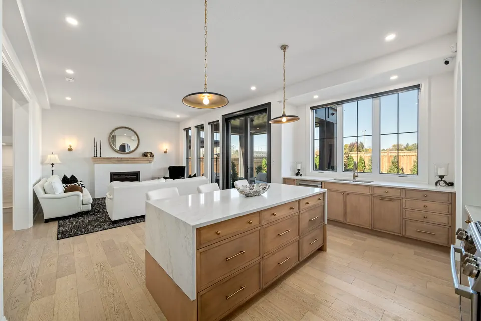 Kitchen island with a waterfall quartz edge, open to the great room, fireplace and black-framed windows