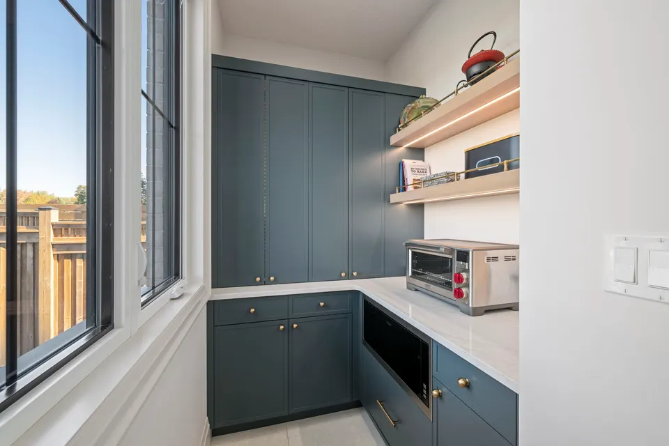 Pantry with navy cabinetry, lit shelves, a built-in microwave and an appliance garage