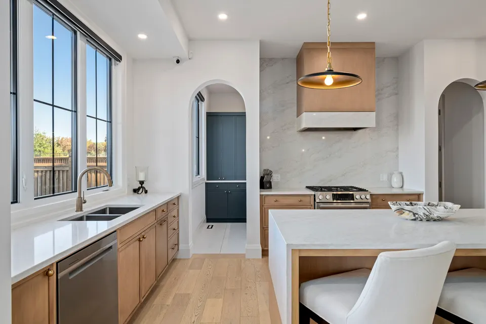 Kitchen sink wall, the range under its hood with a quartz slab backsplash, and the arch to the pantry
