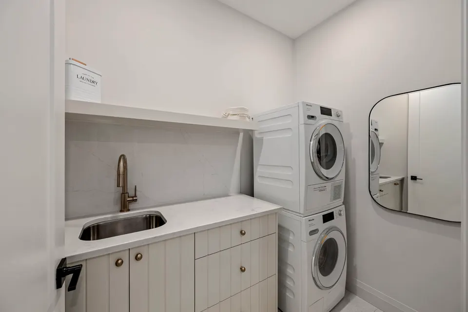 Bedroom-level laundry room with a stacked Miele washer and dryer, sink and quartz counter